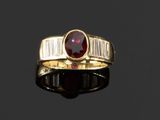 un gros plan sur une bague en or sertie d'une pierre rouge et de diamants taille baguette