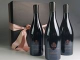 three bottles of red wine in a gift box with a pink ribbon
