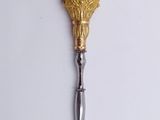 a gold spoon with a knife on it on a white surface