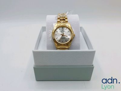 une image représentant une montre en or dans un écrin, posée sur une surface blanche