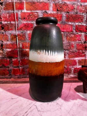 un vase noir et marron posé sur une table devant un mur de briques