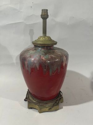 un vase rouge posé sur une table, sur lequel est posée une lampe