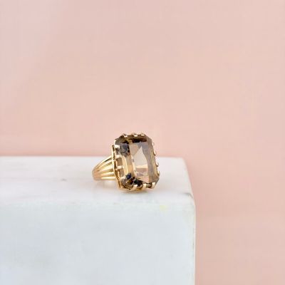 a gold ring with a smoky quartz stone on top of a white marble block
