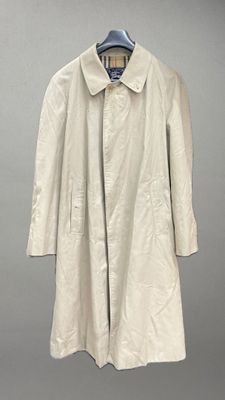 un trench-coat beige suspendu à un cintre sur fond gris