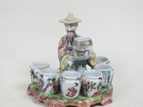 une figurine représentant un homme assis sur un plateau avec des tasses