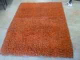 un tapis orange posé au sol dans une pièce où se trouvent des chaises et une table