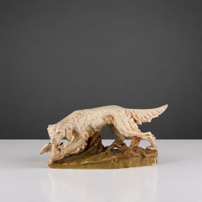 une statue représentant un chien assis sur une bûche, un oiseau dans la gueule