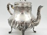 an antique silver teapot with a bird handle on a stand