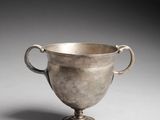 a silver cup with handles on a pedestal on a gray background