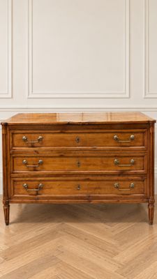 une commode ancienne posée sur un parquet dans une pièce blanche