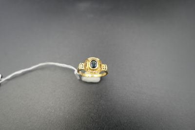 a gold ring with a blue stone sits on a black surface