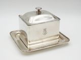 a silverplated butter dish on a tray on a white surface