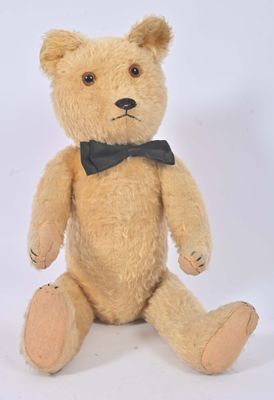un ours en peluche marron avec un nœud papillon, assis sur une surface blanche
