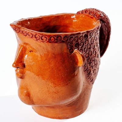 un vase marron orné d'un visage sur un fond blanc