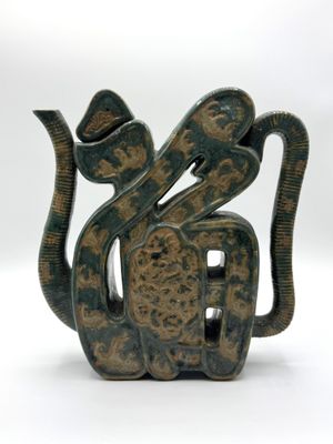 une sculpture représentant un serpent, de couleur verte et marron, posée sur une surface blanche
