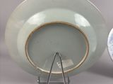 a white plate with a gold rim sitting on a stand next to a clock
