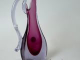 un vase en verre violet et un objet en argent posés sur une surface blanche