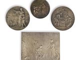 three silver medals of various sizes and shapes on a white surface