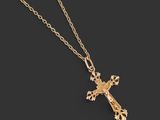 un pendentif en forme de croix en or, suspendu à une chaîne, sur fond noir