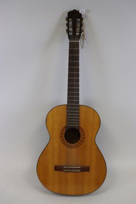 une guitare acoustique posée sur une surface blanche, avec un mur blanc en arrière-plan