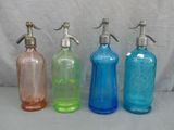 quatre bouteilles en verre de couleurs différentes, munies d'un bec verseur en métal, posées sur une table