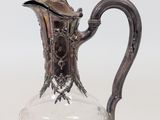 a glass pitcher with a metal handle on a table