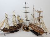 three wooden model ships are sitting on a stand on a white surface