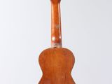 an old wooden guitar hanging from a string on a white wall