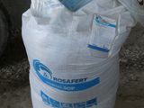 un grand sac de sable posé par terre à côté d'un pneu