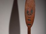 an old wooden paddle with a skull on it sitting next to a shadow of a person