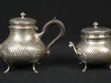 pair of antique silver teapots on stand on black background