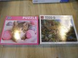 two puzzles are sitting on a table with a cat in the middle of them