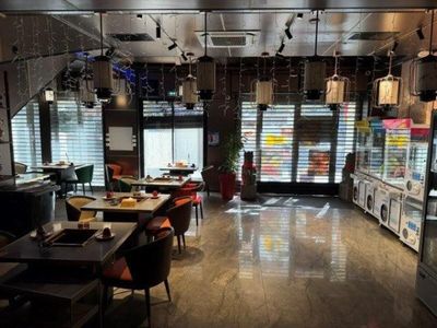 Des tables et des chaises sont alignées dans un restaurant, avec un réfrigérateur en arrière-plan.