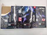 trois boîtes de cartes graphiques Nirox Radeon de la série RX destinées au gaming, posées sur une table