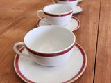 Plusieurs tasses et soucoupes sont alignées sur une table en bois.