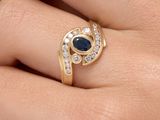 une photo représentant la main d'une femme portant une bague en or sertie d'un saphir bleu et de diamants blancs
