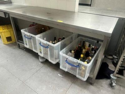 bottles of wine are stored in plastic bins under a stainless steel counter