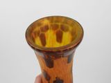 a hand holding a brown and yellow vase against a white background
