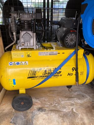 a yellow air compressor sitting in a room with a blue hose