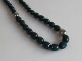 collier composé de perles de verre vertes rehaussées de touches argentées sur un fond blanc