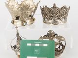 three silver crowns and a green card on a clear table