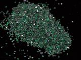 green crystals are scattered on a black surface with a black background