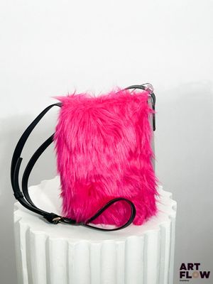 un sac à main rose en fourrure posé sur un socle blanc