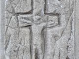 un gros plan d'une croix sur un mur de pierre, avec une personne debout à côté