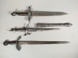 three silver metal swords are displayed on a white surface