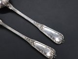 two silver spoons sitting on top of a table next to each other