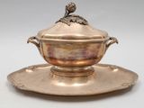 une assiette en argent sur laquelle est posé un oiseau, posée sur une soucoupe
