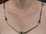the woman is wearing a gold necklace with multi colored stones on it