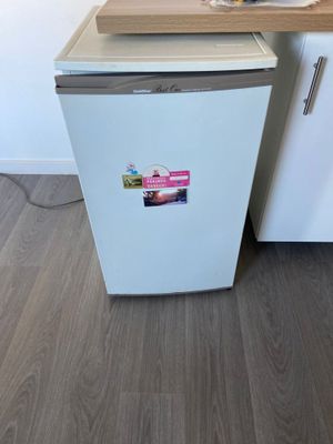 a small white refrigerator in a kitchen with a cutting board on the counter
