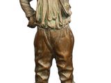 statue en bronze représentant un garçon tenant une batte de baseball, assis sur un rocher